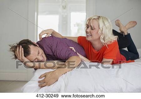 Stock Photo - Playful wife tickling husband on bed. Fotosearch