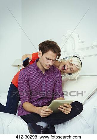 Playful wife with headphones and mp3 player behind husband with digital tablet View Large Photo Image Stock Photo - Playful wife with headphones and mp3 player behind husband with digital tablet. Fotosearch