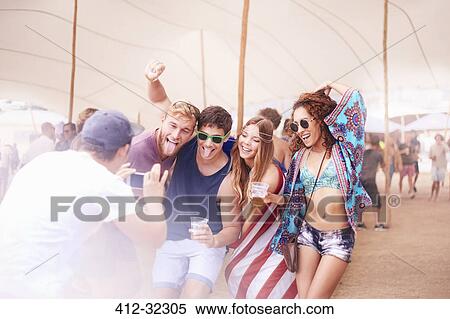 Stock Photography - Playful young friends with beer posing for camera phone at music festival. Fotosearch
