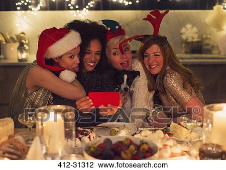 Playful young women with dog taking selfie at Christmas dinner View Large Photo Image Stock Image - Playful young women with dog taking selfie at Christmas dinner. Fotosearch