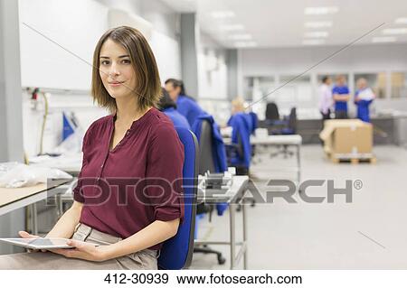 Stock Photo - Portrait confident businesswoman with digital tablet in steel factory office. Fotosearch