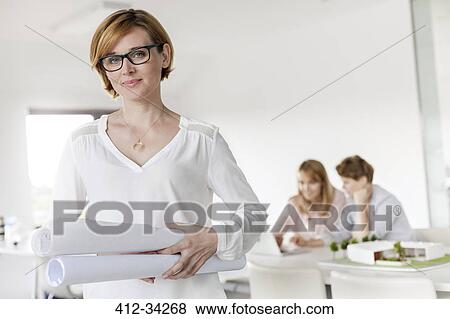 Portrait confident female architect holding blueprints in conference room View Large Photo Image Stock Photo - Portrait confident female architect holding blueprints in conference room. Fotosearch