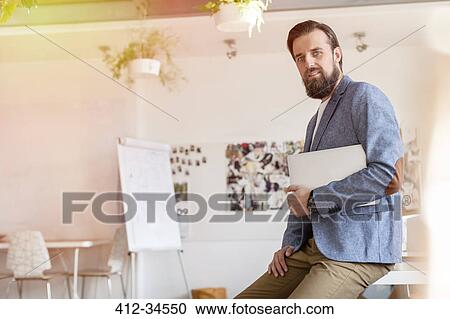Stock Image - Portrait confident male design professional holding laptop in office. Fotosearch