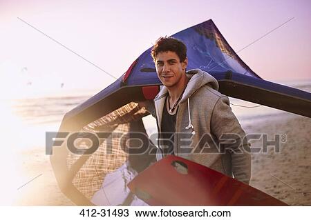Stock Image - Portrait confident man carrying kiteboard equipment on beach. Fotosearch