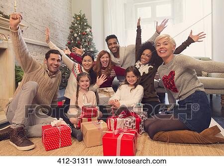 Stock Image - Portrait enthusiastic family and friends with Christmas gifts in living room. Fotosearch