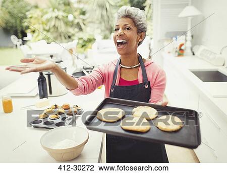 Stock Image - Portrait enthusiastic mature woman baking cookies and kitchen. Fotosearch