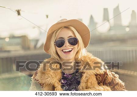 Portrait enthusiastic young woman wearing hat and sunglasses on sunny rooftop View Large Photo Image Stock Image - Portrait enthusiastic young woman wearing hat and sunglasses on sunny rooftop. Fotosearch