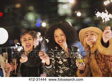 Picture - Portrait enthusiastic young women waving sparklers at party. Fotosearch