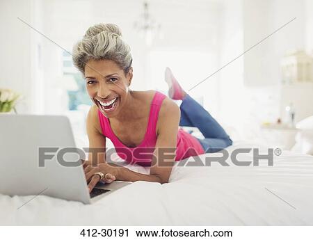 Portrait laughing mature woman using laptop on bed View Large Photo Image Stock Image - Portrait laughing mature woman using laptop on bed. Fotosearch