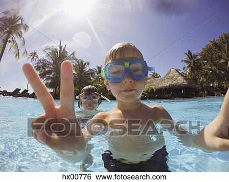 Stock Photograph - Portrait of boy gesturing peace sign in tropical swimming pool. Fotosearch
