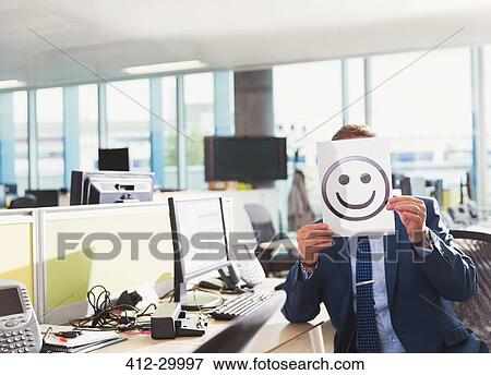 Portrait of businessman holding smiley face printout over his face in office View Large Photo Image Stock Photo - Portrait of businessman holding smiley face printout over his face in office. Fotosearch