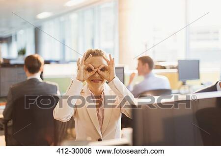 Portrait of playful businesswoman pretending to wear glasses at desk in office View Large Photo Image Stock Photograph - Portrait of playful businesswoman pretending to wear glasses at desk in office. Fotosearch