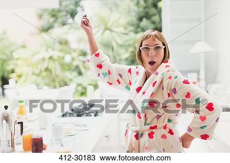 Stock Image - Portrait of playful mature woman in bathrobe dancing in kitchen. Fotosearch
