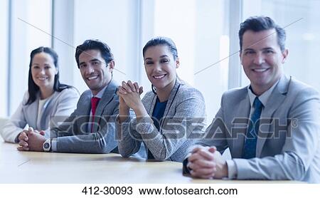Stock Image - Portrait of smiling business people sitting in a row in conference room. Fotosearch