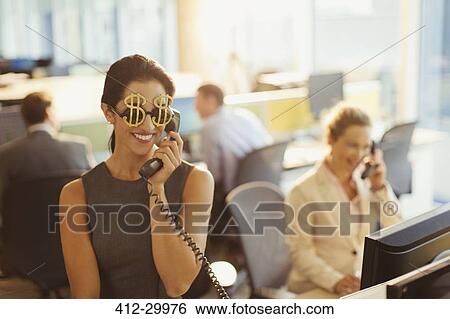 Portrait of smiling businesswoman wearing dollar sign sunglasses answering telephone in office View Large Photo Image Stock Photograph - Portrait of smiling businesswoman wearing dollar sign sunglasses answering telephone in office. Fotosearch