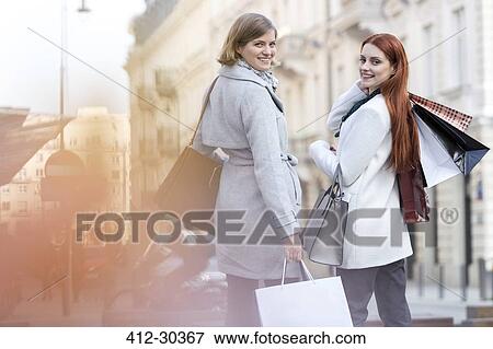 Stock Photo - Portrait of smiling women with shopping bags on city sidewalk. Fotosearch