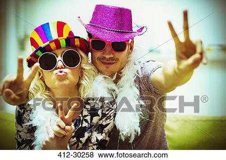 Stock Photo - Portrait playful couple in costume sunglasses and hats gesturing peace sign. Fotosearch