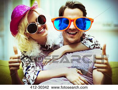 Stock Image - Portrait playful couple wearing costume sunglasses and hat gesturing thumbs-up. Fotosearch