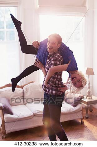 Portrait playful husband carrying wife over shoulder in living room View Large Photo Image Stock Photo - Portrait playful husband carrying wife over shoulder in living room. Fotosearch