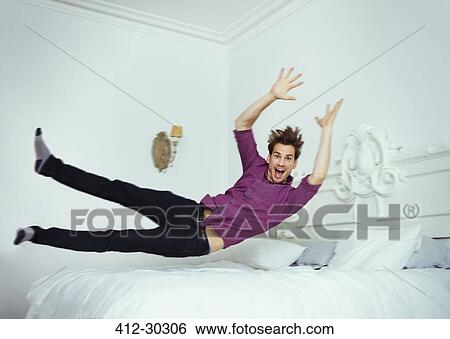 Stock Photograph - Portrait playful man jumping onto bed. Fotosearch