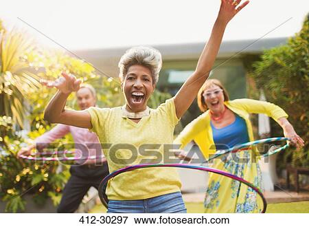 Stock Photo - Portrait playful mature adults spinning with plastic hoops in garden. Fotosearch