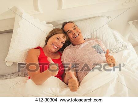 Portrait playful mature couple gesturing thumbs-up in bed View Large Photo Image Picture - Portrait playful mature couple gesturing thumbs-up in bed. Fotosearch