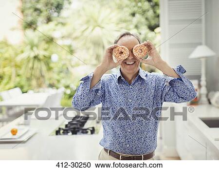 Portrait playful mature man covering eyes with donuts View Large Photo Image Stock Image - Portrait playful mature man covering eyes with donuts. Fotosearch