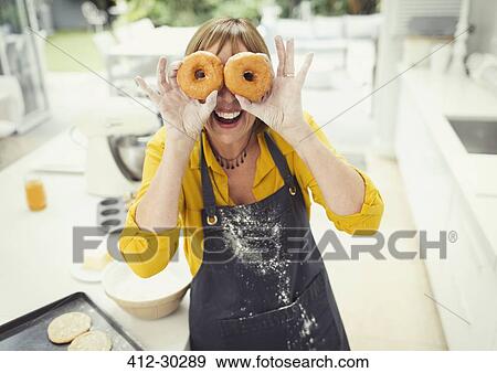 Portrait playful mature woman covering eyes with donuts in kitchen View Large Photo Image Stock Photo - Portrait playful mature woman covering eyes with donuts in kitchen. Fotosearch