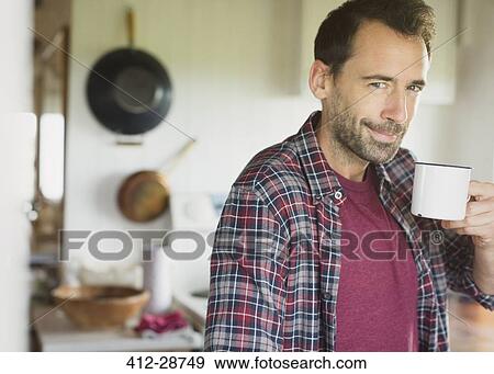 Stock Photo - Portrait smiling brunette man drinking coffee in kitchen. Fotosearch