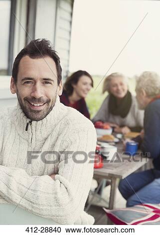 Portrait smiling brunette man in sweater on porch with family in background View Large Photo Image Stock Image - Portrait smiling brunette man in sweater on porch with family in background. Fotosearch