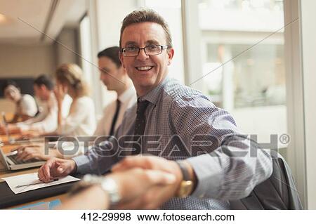 Stock Photo - Portrait smiling businessman handshaking in conference room meeting. Fotosearch
