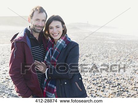 Portrait smiling couple hugging on sunny rocky beach View Large Photo Image Picture - Portrait smiling couple hugging on sunny rocky beach. Fotosearch