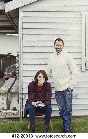 Stock Photo - Portrait smiling couple in sweaters drinking coffee outside house. Fotosearch