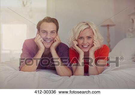 Stock Photograph - Portrait smiling couple with head in hands on bed. Fotosearch