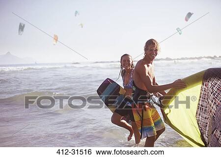 Portrait smiling couple with kiteboarding equipment in ocean surf View Large Photo Image Stock Photograph - Portrait smiling couple with kiteboarding equipment in ocean surf. Fotosearch