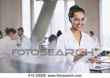 Stock Photo - Portrait smiling female college student taking notes in science laboratory classroom. Fotosearch