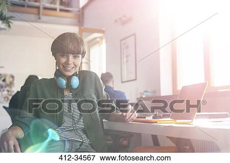 Portrait smiling female design professional with headphones at laptop in office View Large Photo Image Stock Photo - Portrait smiling female design professional with headphones at laptop in office. Fotosearch