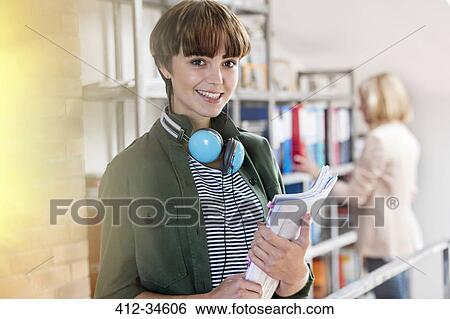 Stock Photograph - Portrait smiling female design professional with headphones holding paperwork in design library. Fotosearch