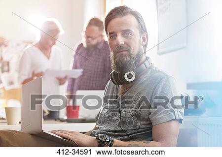 Portrait smiling male design professional with headphones using laptop in office View Large Photo Image Stock Image - Portrait smiling male design professional with headphones using laptop in office. Fotosearch