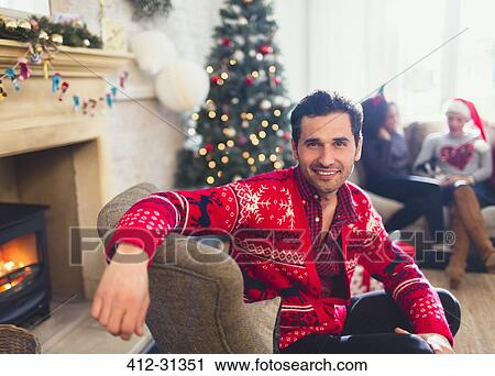 Stock Image - Portrait smiling man in Christmas sweater sitting in living room. Fotosearch
