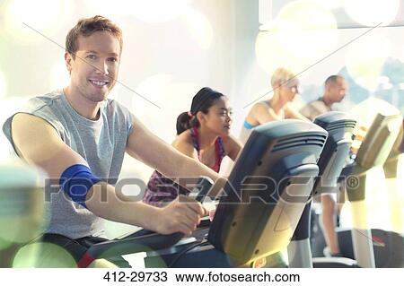 Stock Image - Portrait smiling man riding exercise bike at gym. Fotosearch