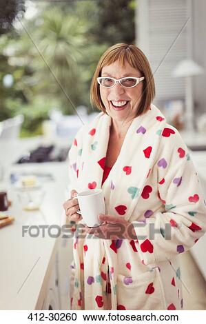 Stock Image - Portrait smiling mature woman drinking coffee in bathrobe. Fotosearch