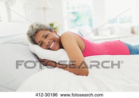 Stock Photograph - Portrait smiling mature woman laying on bed. Fotosearch