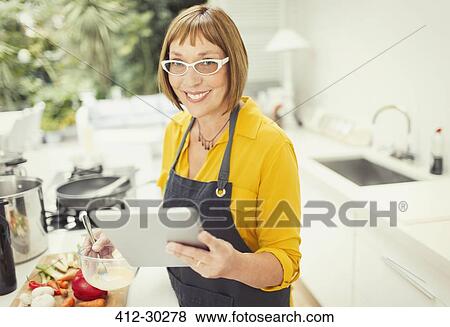 Stock Photo - Portrait smiling mature woman with digital tablet cooking in kitchen. Fotosearch