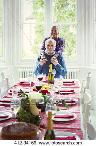 Stock Photo - Portrait smiling multi-ethnic senior couple at Christmas dinner table. Fotosearch