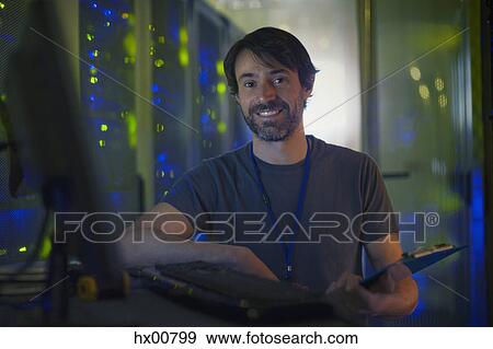 Stock Photo - Portrait smiling server room technician with clipboard at computer. Fotosearch