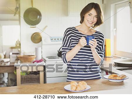 Stock Image - Portrait smiling woman drinking coffee in kitchen. Fotosearch