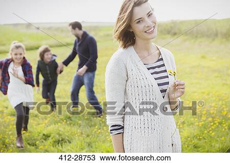 Stock Image - Portrait smiling woman holding wildflower in meadow with family. Fotosearch