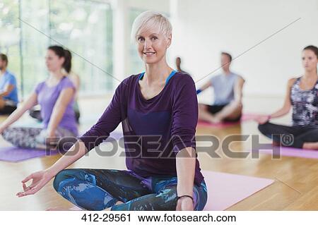 Stock Image - Portrait smiling woman sitting in lotus position in yoga class. Fotosearch