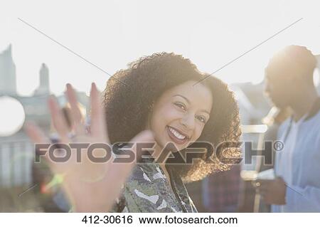Stock Photograph - Portrait smiling woman waving at rooftop party. Fotosearch